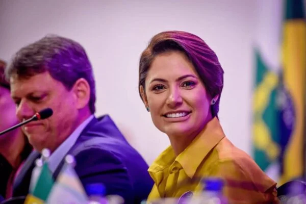 Imagem colorida mostra Michelle Bolsonaro, mulher branca, de cabelos castanhos. curtos, de camisa amarela, em imagem dos ombros para cima PT Lula