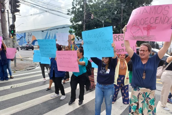 Imagem colorida de professoras segurando cartazes de protesto. Metrópoles
