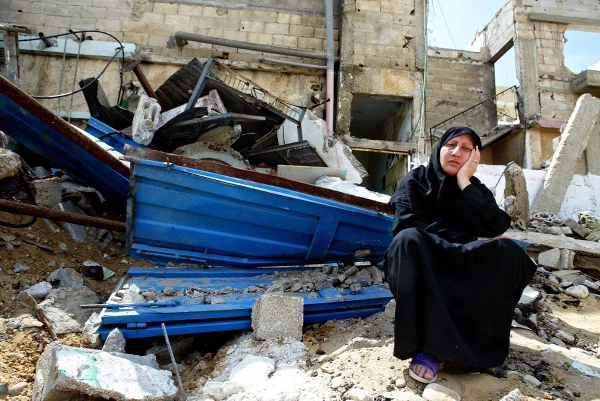 Imagem colorida mostra mulher palestina sentada em escombros na Faixa de Gaza - Metrópoles