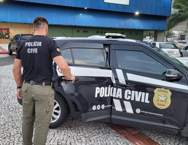 Agente da polícia civil do estado de santa catarina aparece abrindo a porta traseira de uma viatura - Metrópoles