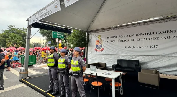 Três policiais militares fardadas estão de pé em frente a uma tenda de atendimento à vítimas de assédio
