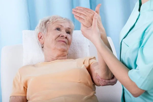 Mulher de jaleco segura braço de senhora com osteoroporose deitada - Metrópoles
