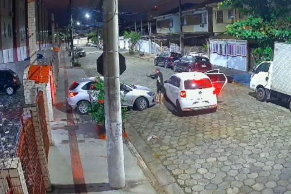Imagem colorida mostra dois assaltantes, irmãos, parando um carro em frente a um prédio. Um deles está com um revólver e mira o motorista do carro - Metrópoles