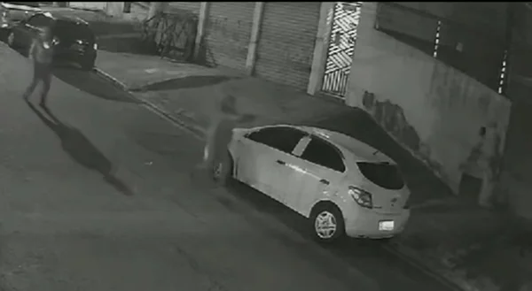 Imagem em preto e branco mostra dois homens apontando a arma a um empresário; o tiro acertou as costas da vítima - Metrópoles