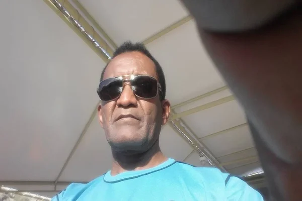 Homem negro de óculos, vestido de blusa azul - Metrópoles