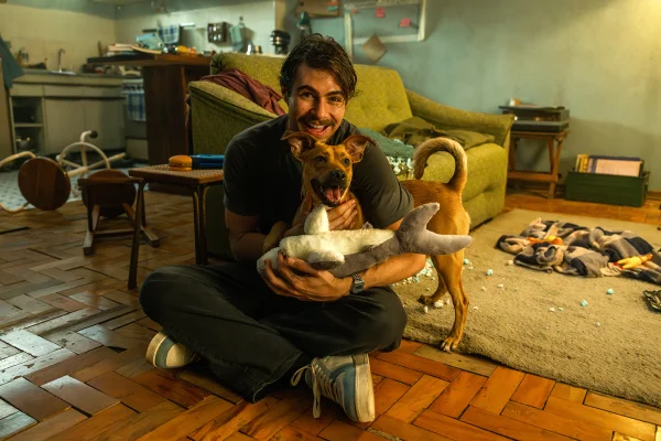 Imagem colorida de Rafa Vitti sorrindo para a foto com o cachorro Amendoim, no set de Caramelo, da Netflix