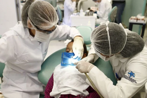 Imagem colorida mostra dentistas tratando inflamação na boca de um paciente - Metrópoles