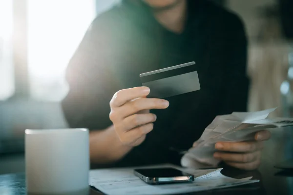 Imagem de pessoa segurando o cartão de crédito com uma mão e as contas com outra - Metrópoles