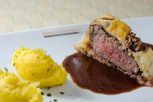 Imagem colorida de uma fatia de bife Wellington e um acompanhamento