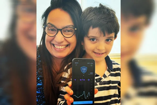 Foto mostra mulher adulta sorrindo ao lado de menino jovem. Ele mostra em seu celular os índices glicêmicos para controle de diabetes