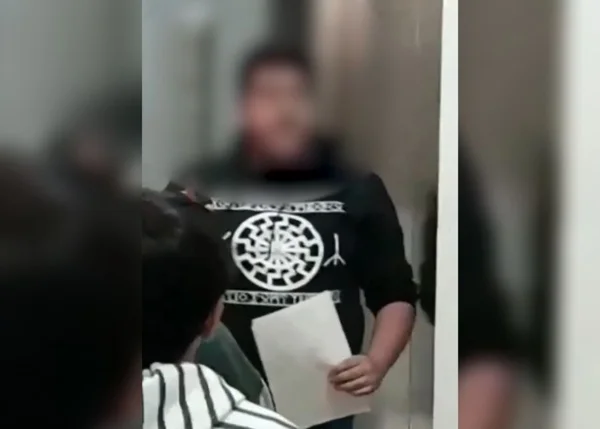 foto colorida de homem com casaco preto e simbolo nazista branco ao meio