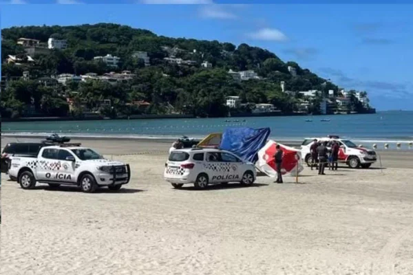 Duas viaturas brancas estão próximas a corpo caído em faixa de areia - Metrópoles
