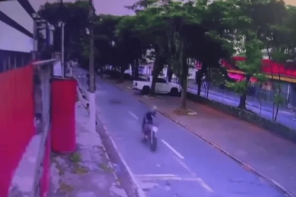 Imagem colorida de uma câmera de segurança mostra dois homens fugindo de motocicleta em uma rua, quando um dos indivíduos cai da garupa da moto - Metrópoles