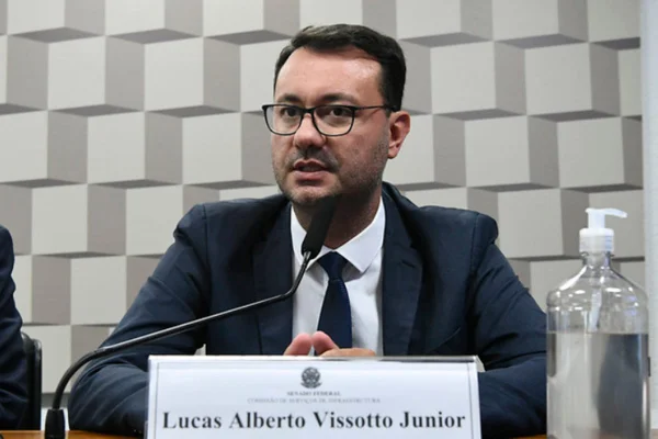 Foto colorida de homem de cabelo curto com óculos e terno