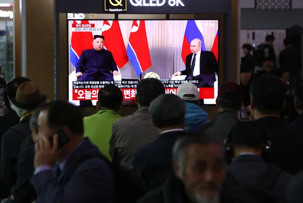 Foto colorida de pessoas assistindo pela televisão o encontro entre Kim Jong-un e Putin - Metrópoles