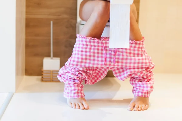 Fotografia colorida. Mulher usa privada e segura papel nas mãos