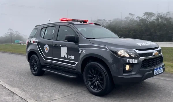 Imagem mostra veículo policial, cinza, com farol aceso, em rodovia
