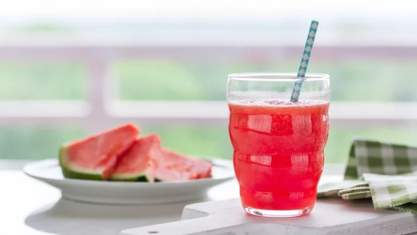 Copo com suco de melancia e fatias ao lado