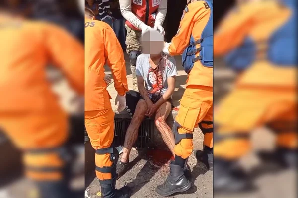 imagem colorida. Jovem ensanguentado sentado no chão sendo atendido por bombeiros