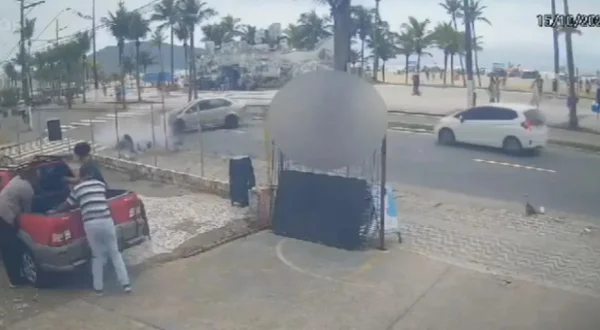 Imagem colorida mostra carro batido em moto e o motociclista voando em direção ao poste em avenida perto de uma praia - Metrópoles