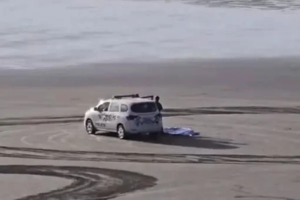Imagem colorida de carro da PM em cima da areia ao lado de corpo de homem - Metrópoles