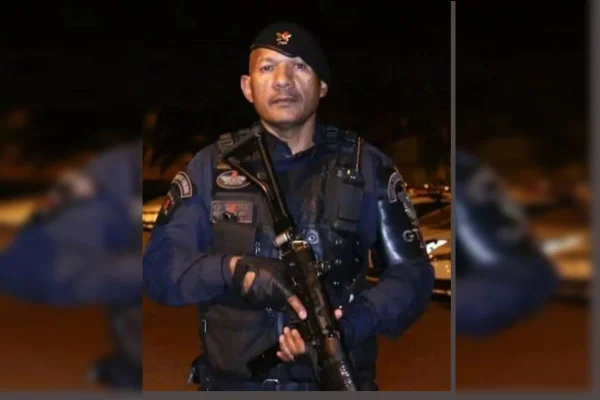 PM de preto segurando uma pistola e olhando para a câmera