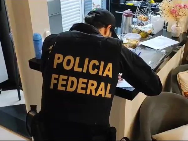 Foto colorida mostra agente da PF escrevendo em caderno, de costas