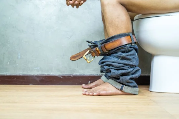 Imagem mostra pernas de homem sentado no vaso sanitário - Metrópoles