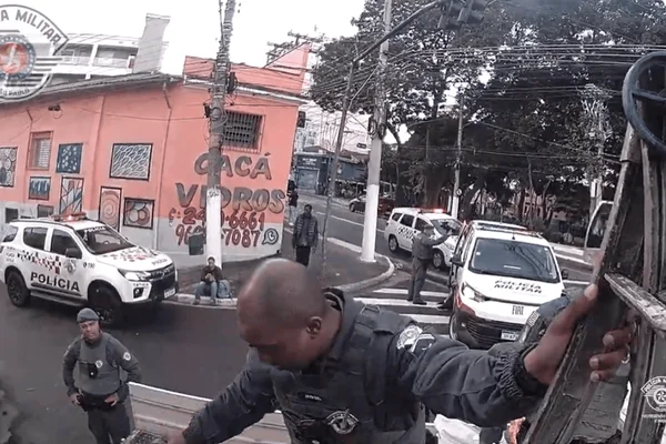 Imagem colorida de policial militar ajudando passageiros a pularem muro que cerca trilhos da linha 12-Safira - Metrópoles