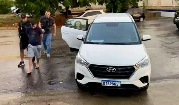 Momento em Polícia Civil do Distrito Federal prende homens que furtavam cartões de idosos em área nobre do Distrito Federal. Um policial armado conduz os dois homens para fora de um carro - Metrópoles