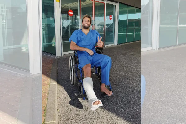 Imagem colorida mostra Frederico Morais, surfista português, com o pé imobilizado em frente a uma fachada de hospital | Metrópoles