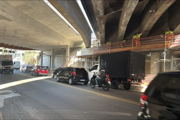 Trecho de avenida sob viaduto, onde carros trafegam e trabalhadores realizam obra - Metrópoles