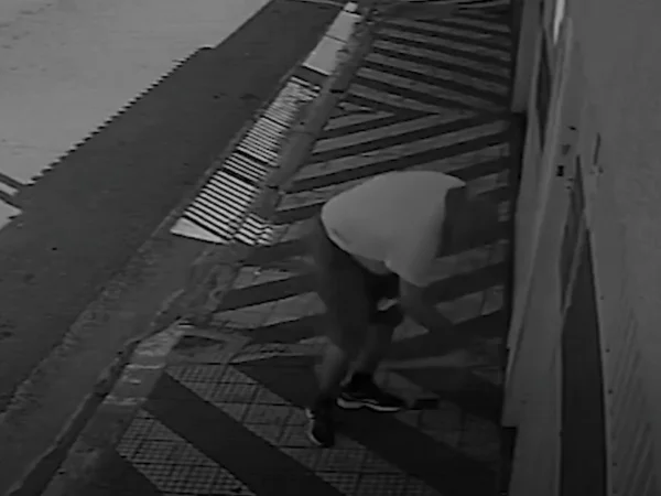 Foto em preto e branco mostra homem abaixado jogando objeto para dentro de portão