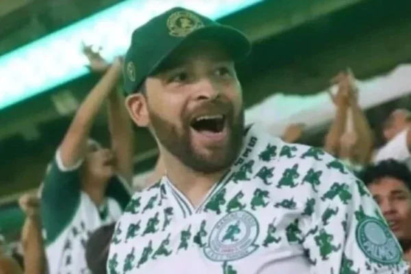 Homem branco de barba, com a boca aberta, e boné verde e camiseta de torcida organizada verde - Metrópoles