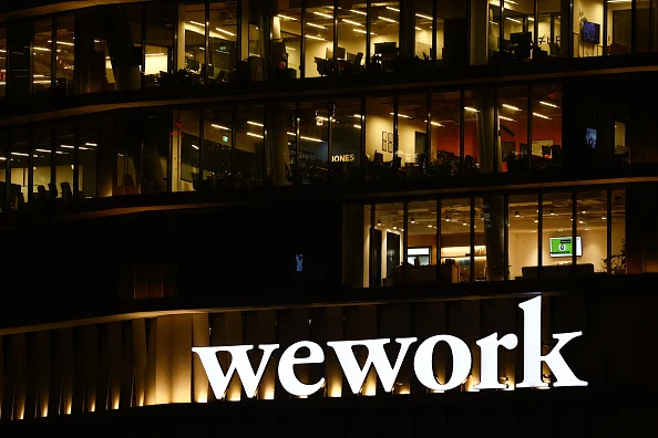 Imagem de escritório com o logotipo da WeWork em letras brancas e funcionários trabalhando com as luzes acesas em diversas salas - Metrópoles