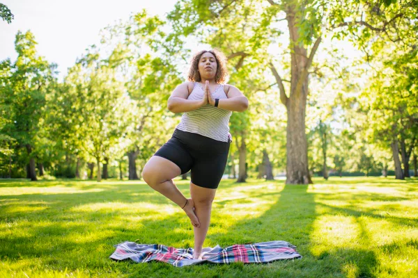Imagem mostra mulher em um parque fazendo uma posição de ioga de pé - Metrópoles