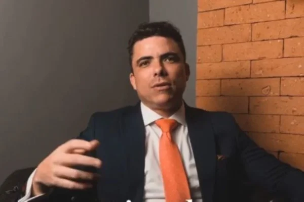 Imagem colorida de um advogado, homem branco com olhos olhos azuis, vestido com paletó preto e gravata laranja - Metrópoles