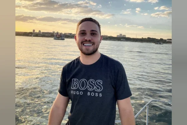 Imagem colorida de homem com camisa preto, com um lago no fundo