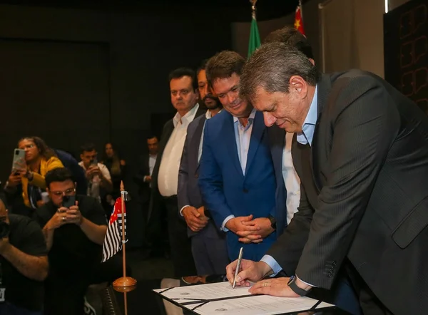 Fotografia colorida mostra Arthur Lima observando Tarcísio de Freitas assinar um documento - Metrópoles