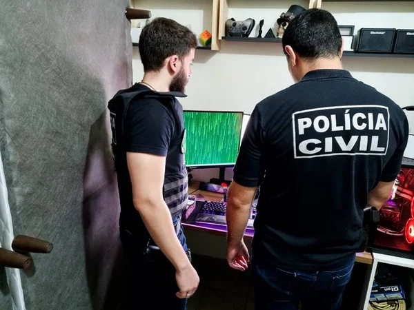 Dois agentes da PCDF de costas, com computador ligado e tela verde