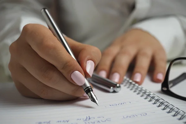 Na foto, a mão de uma mulher escrevendo em um caderno as resoluções de Ano-Novo - Metrópoles