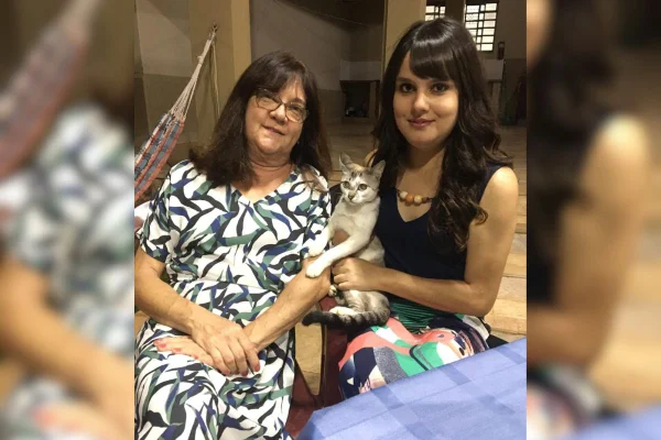 Imagem colorida de mãe e filha sentadas uma do lado da outro com gato no colo - Metrópoles