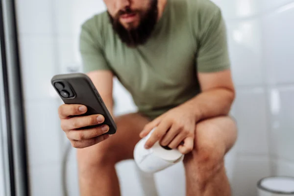 Homem usando o banheiro com o celular na mão