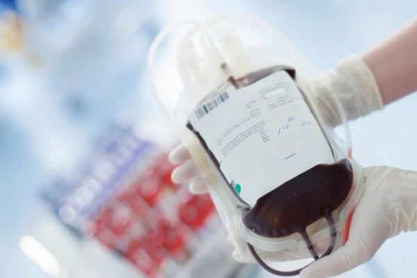 Imagem colorida de mão com luvas segurando bolsa de sangue - Metrópoles
