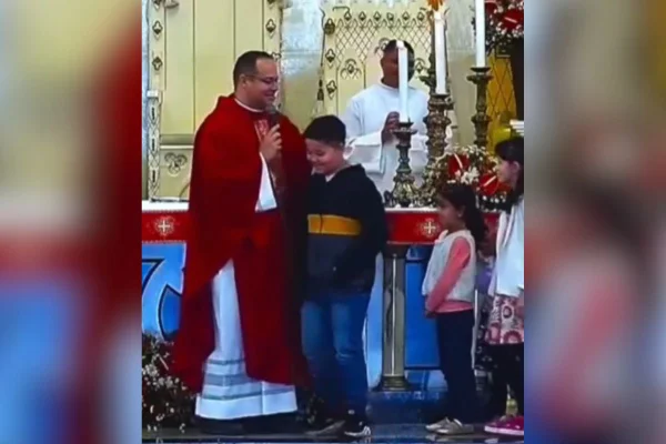 Imagem colorida mostra padre com microfone na mão e uma fila de crianças dentro de igreja no interior de São Paulo - Metrópoles