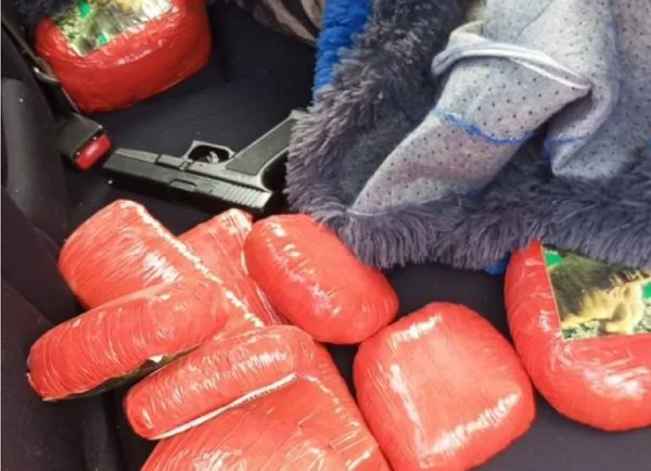 Colombiana Imagem colorida mostra pacotes de maconha na cor rosa e um simulacro de arma de fogo no banco traseiro de um carro - Metrópoles