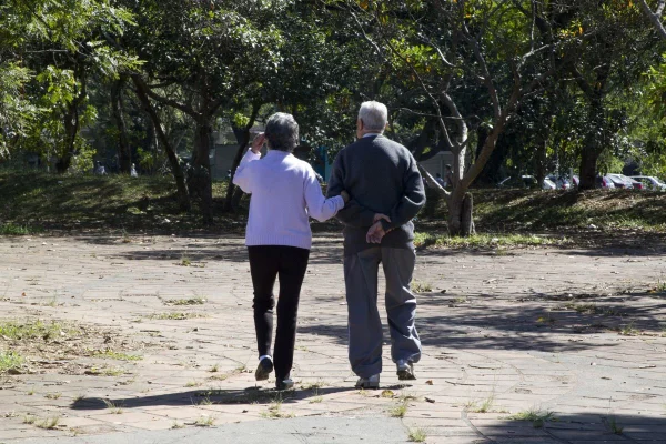 Imagem colorida mostra casal de idosos de costas, caminhando de braços entrelaçados - Metrópoles