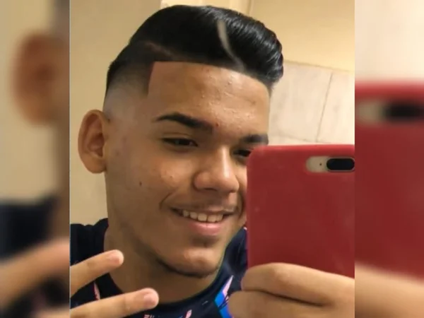 Imagem de jovem negro sorrindo com celular vermelho na mão - Metrópoles