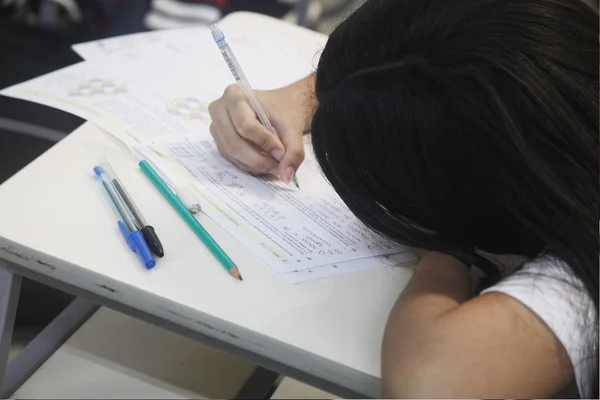 Foto colorida de uma estudante branca com cabelos escuros realizando a prova da 2ª fase da Obmep 2022 - Metrópoles