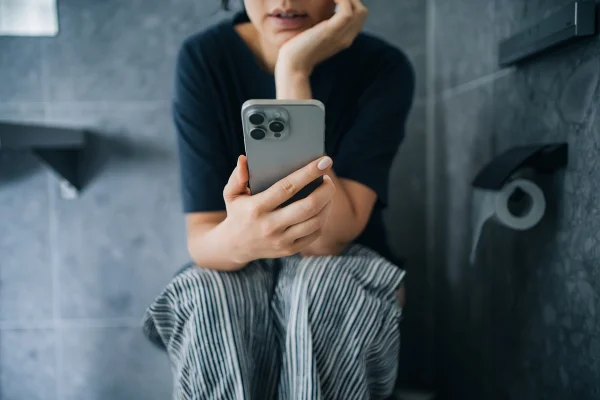 Mulher sentada em vaso sanitário mexendo no celular - Metrópoles